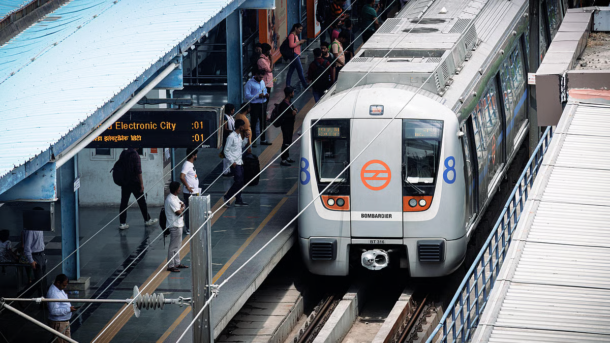 Delhi Metro train at a busy metro station platform with passengers waiting, featuring the Delhi Metro logo and electronic signboard displaying train timings, illustrating Delhi news live on the latest Delhi Metro fare hike and metro service updates.