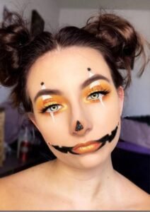 Girl with orange and green pumpkin-inspired halloween makeup design for a fun festive look.