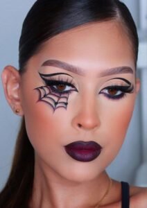 Halloween makeup design featuring black spider web drawn near the eyes with silver glitter highlights.