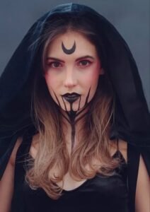 Woman with bold witch-inspired halloween makeup design in green and purple shades with glitter finish.