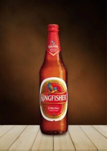 A brown glass bottle of Kingfisher Strong Premium Beer, with the classic Kingfisher bird logo prominently displayed, placed on a light wooden table, highlighting one of the oldest Indian Beer Brands.