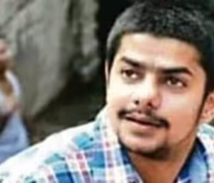 Close-up headshot of a young man with a mustache wearing a plaid shirt, identified as an associate or image related to Anmol Bishnoi in the ongoing gang investigation.