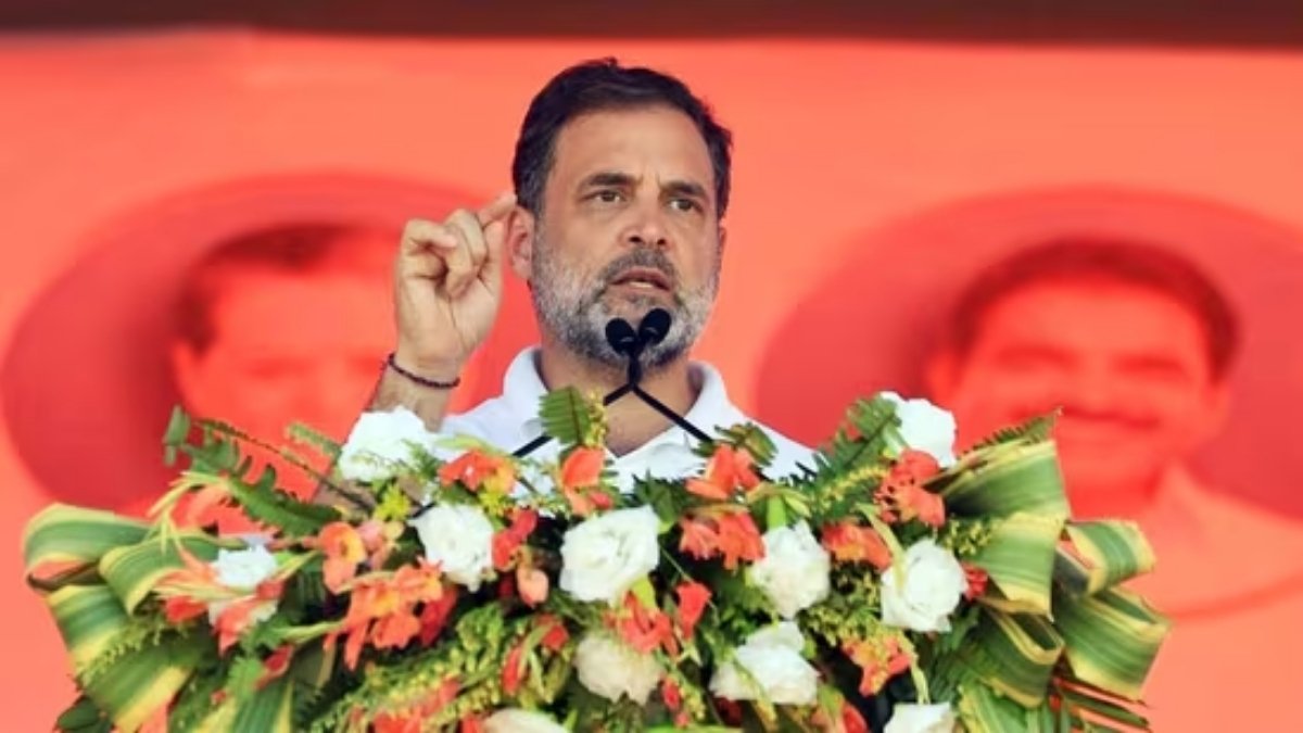 Indian politician Rahul Gandhi speaking passionately at a podium decorated with orange and white flowers during a political rally, central to today's political **NEWS** headlines.