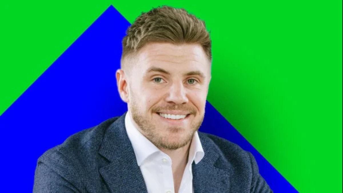 A smiling, light-skinned man with short brown hair and a stubble beard, wearing a dark blue blazer over a white shirt, set against a geometric background of bright green and blue. The background colors are bold and non-standard for a business portrait. This individual is associated with Wingstop.