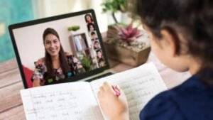 Student taking notes during a virtual lesson with a teacher and classmates on screen, as schools are closed.