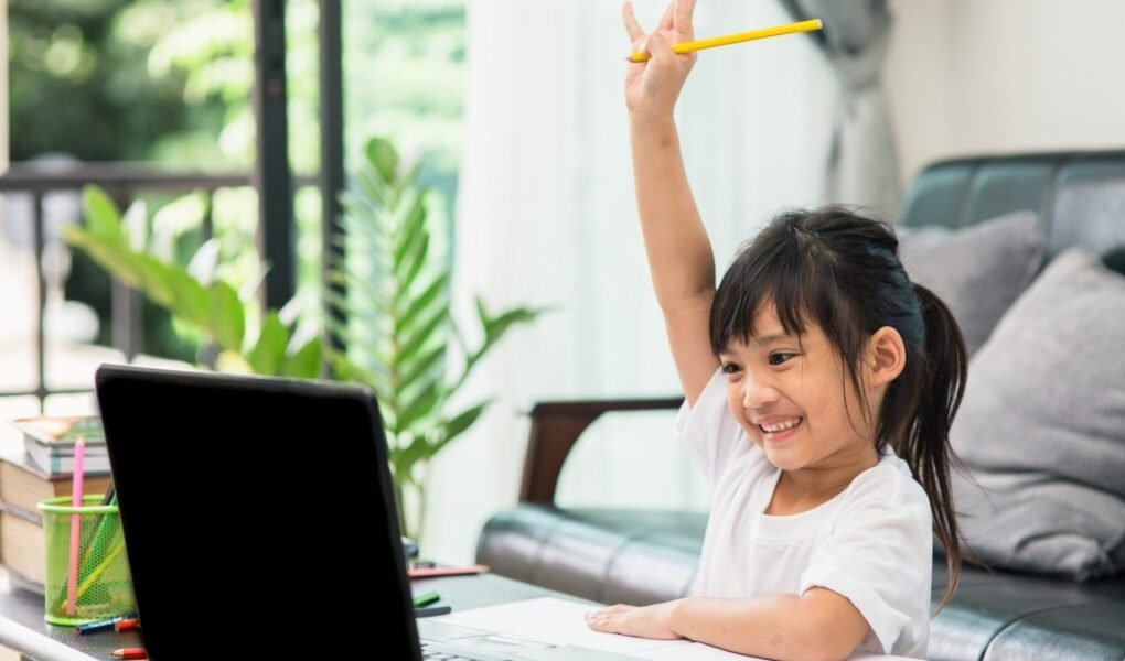 Happy young student raises hand during online class, emphasizing that schools are closed but learning continues.
