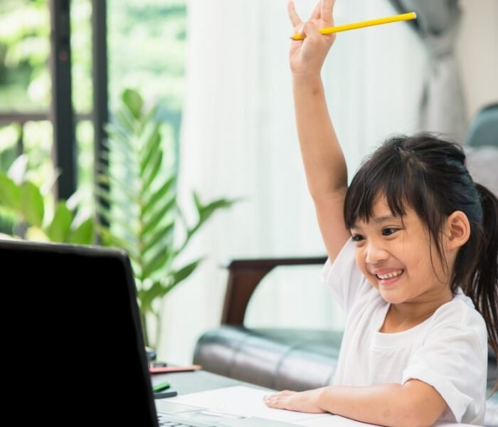 Happy young student raises hand during online class, emphasizing that schools are closed but learning continues.