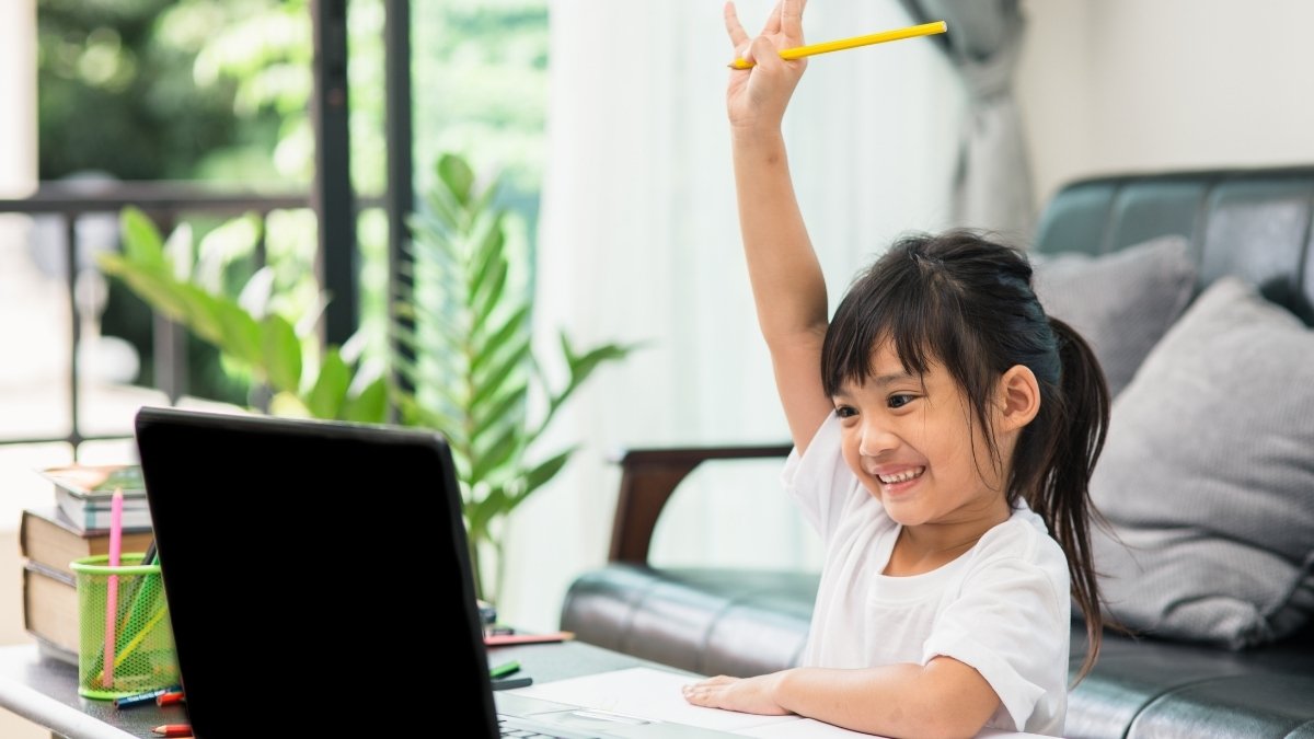Happy young student raises hand during online class, emphasizing that schools are closed but learning continues.