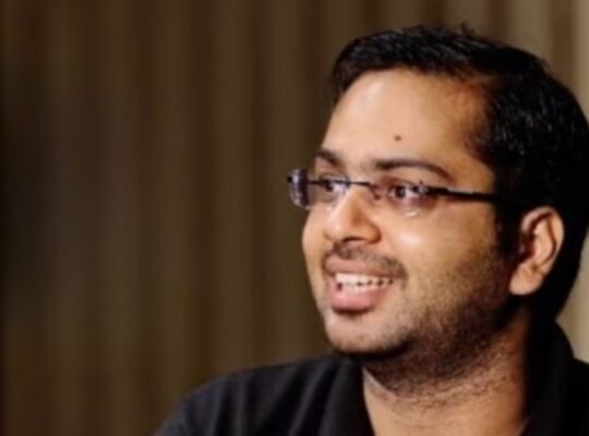 Close-up headshot of the IITian CEO, wearing glasses and a black shirt, smiling while discussing the **trending** topic of paying a high salary for a home manager.