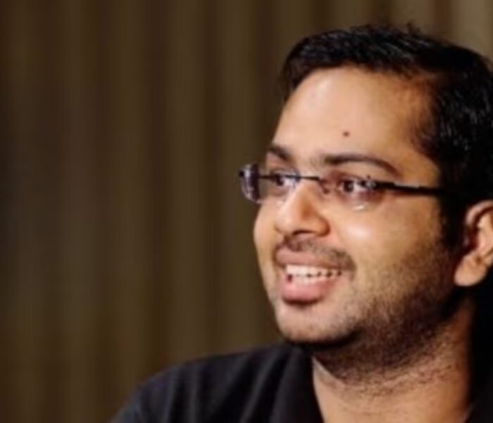 Close-up headshot of the IITian CEO, wearing glasses and a black shirt, smiling while discussing the **trending** topic of paying a high salary for a home manager.