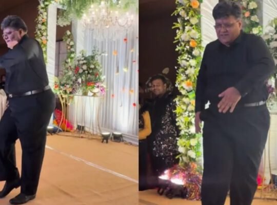 An elderly father dressed in all black performing a humorous slow-motion dance on stage at his daughter's Sangeet ceremony, the moment captured in a viral **Video** clip.
