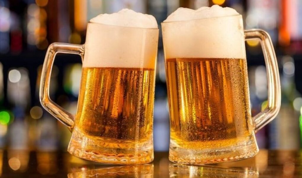 wo frosted glass mugs of golden lager, topped with a thick layer of white foam, clinking in a dimly lit bar setting, representing the **BEST BEER BRANDS IN INDIA** and celebration