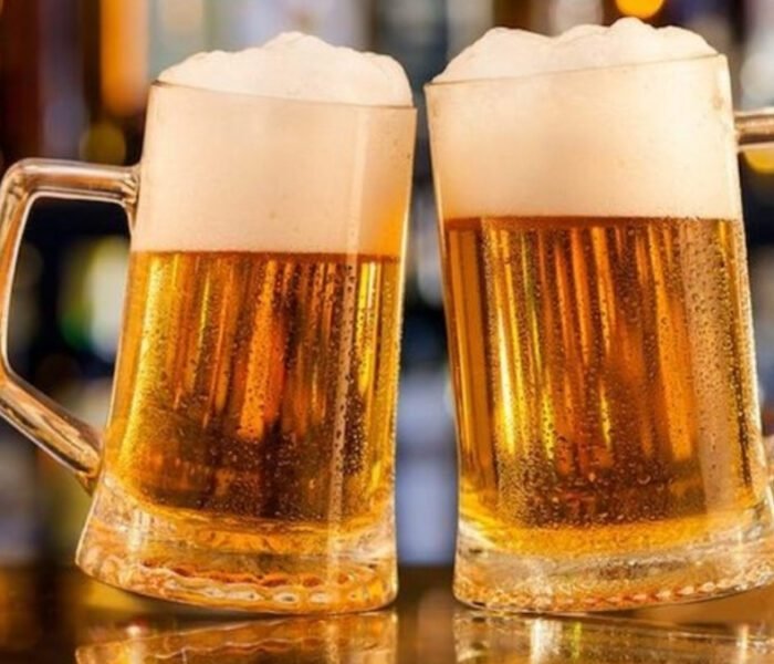 wo frosted glass mugs of golden lager, topped with a thick layer of white foam, clinking in a dimly lit bar setting, representing the **BEST BEER BRANDS IN INDIA** and celebration