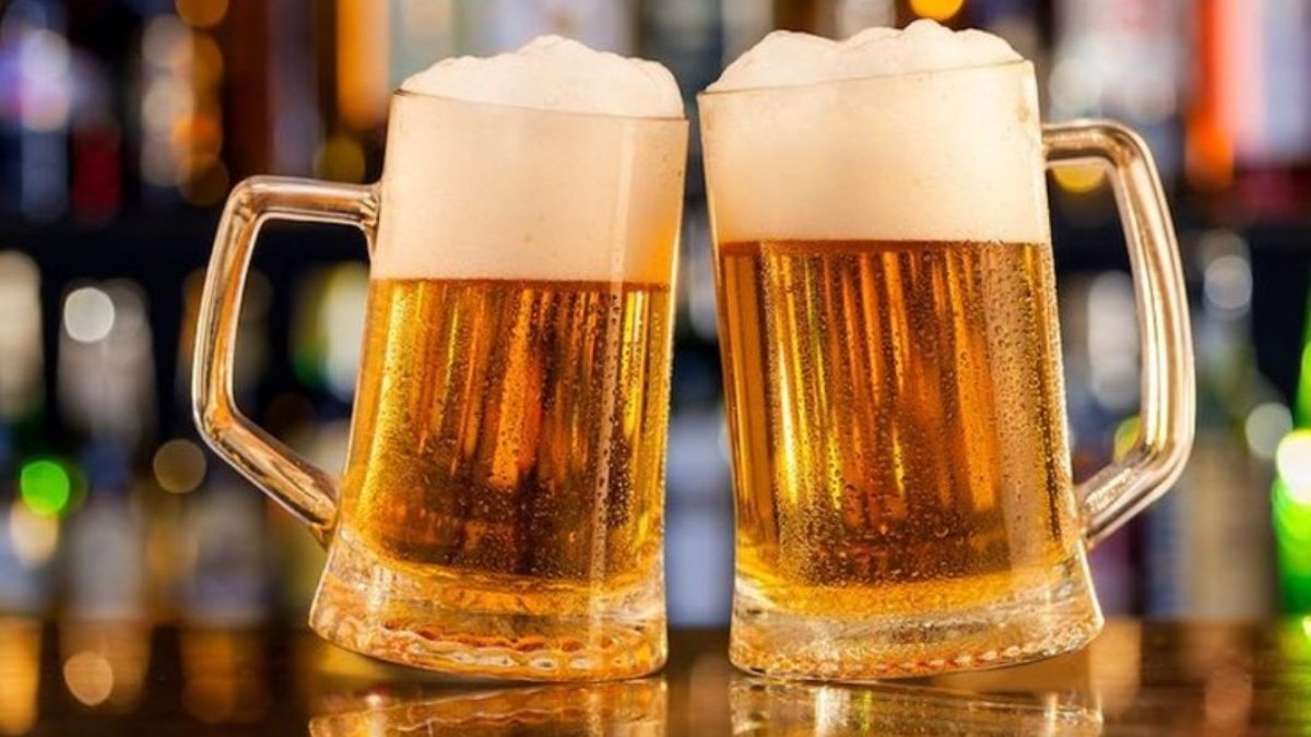 wo frosted glass mugs of golden lager, topped with a thick layer of white foam, clinking in a dimly lit bar setting, representing the **BEST BEER BRANDS IN INDIA** and celebration