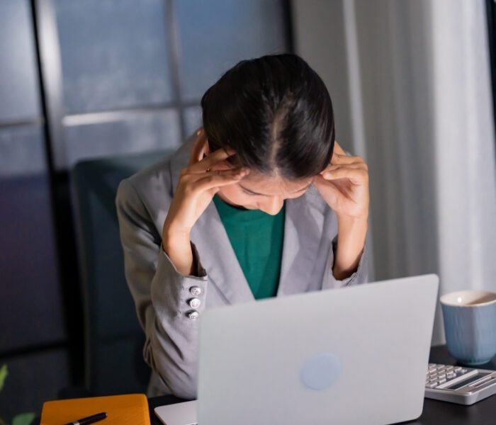 Employee holding head in stress, illustrating workplace toxicity and corporate work pressure