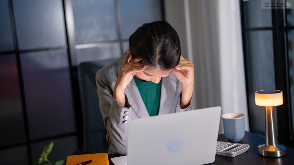Employee holding head in stress, illustrating workplace toxicity and corporate work pressure